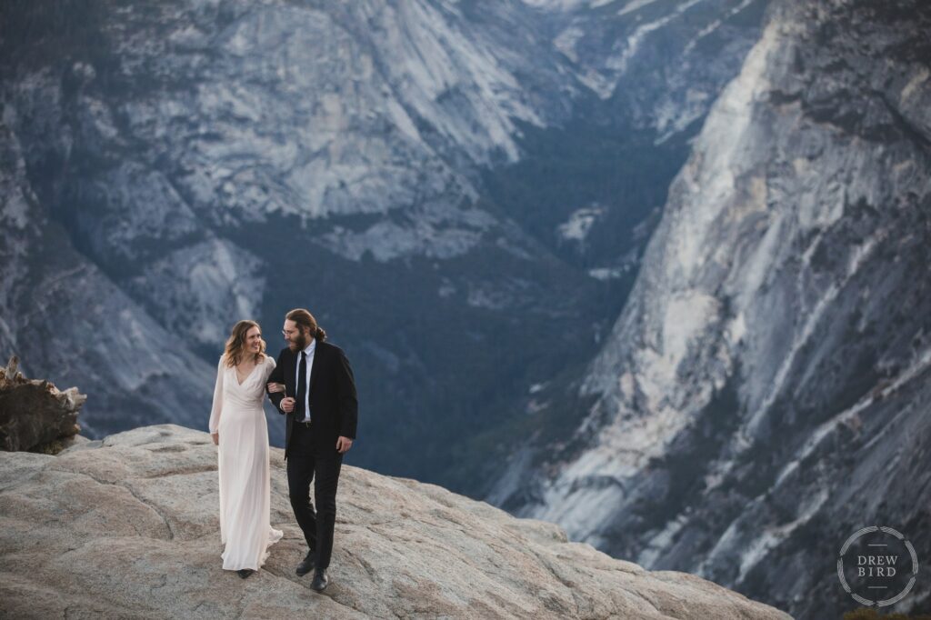 Bride and groom walk on cliff edge at glacier point. Yosemite National Park wedding elopement. Oakland micro wedding photographer Drew Bird.