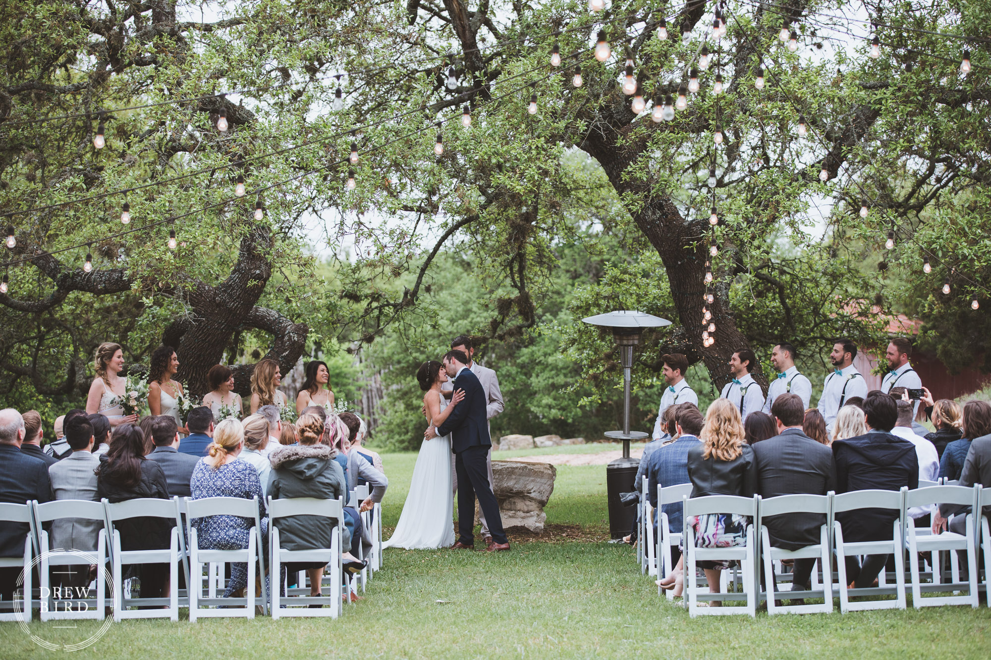 Bride and groom kiss during wedding ceremony under trees. Austin Texas ranch wedding. Outdoor rustic ranch wedding photography.
