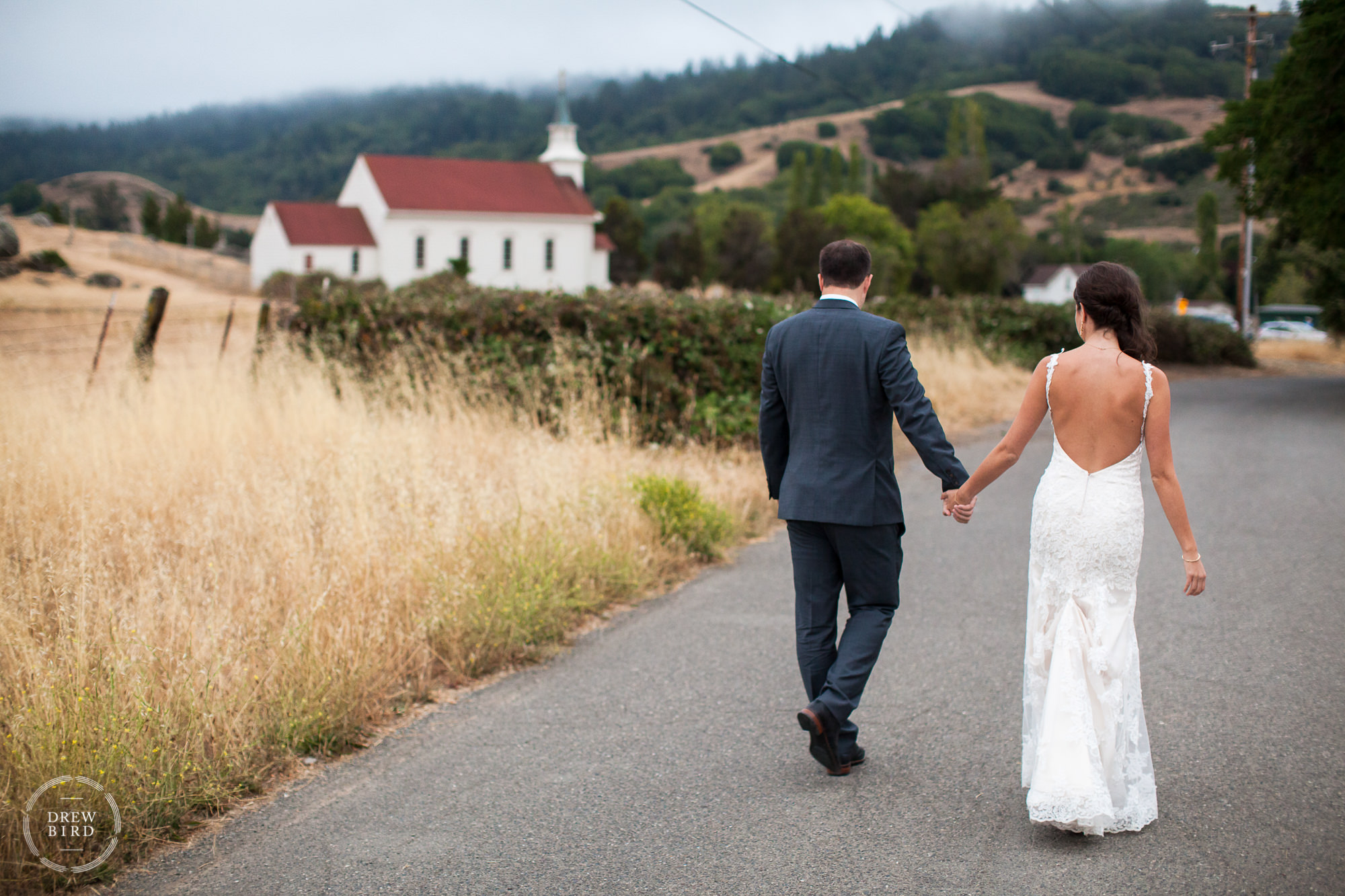 Bride and groom holding hands walking down country road. Rancho Nicasio rustic wedding venue in Marin County, California.