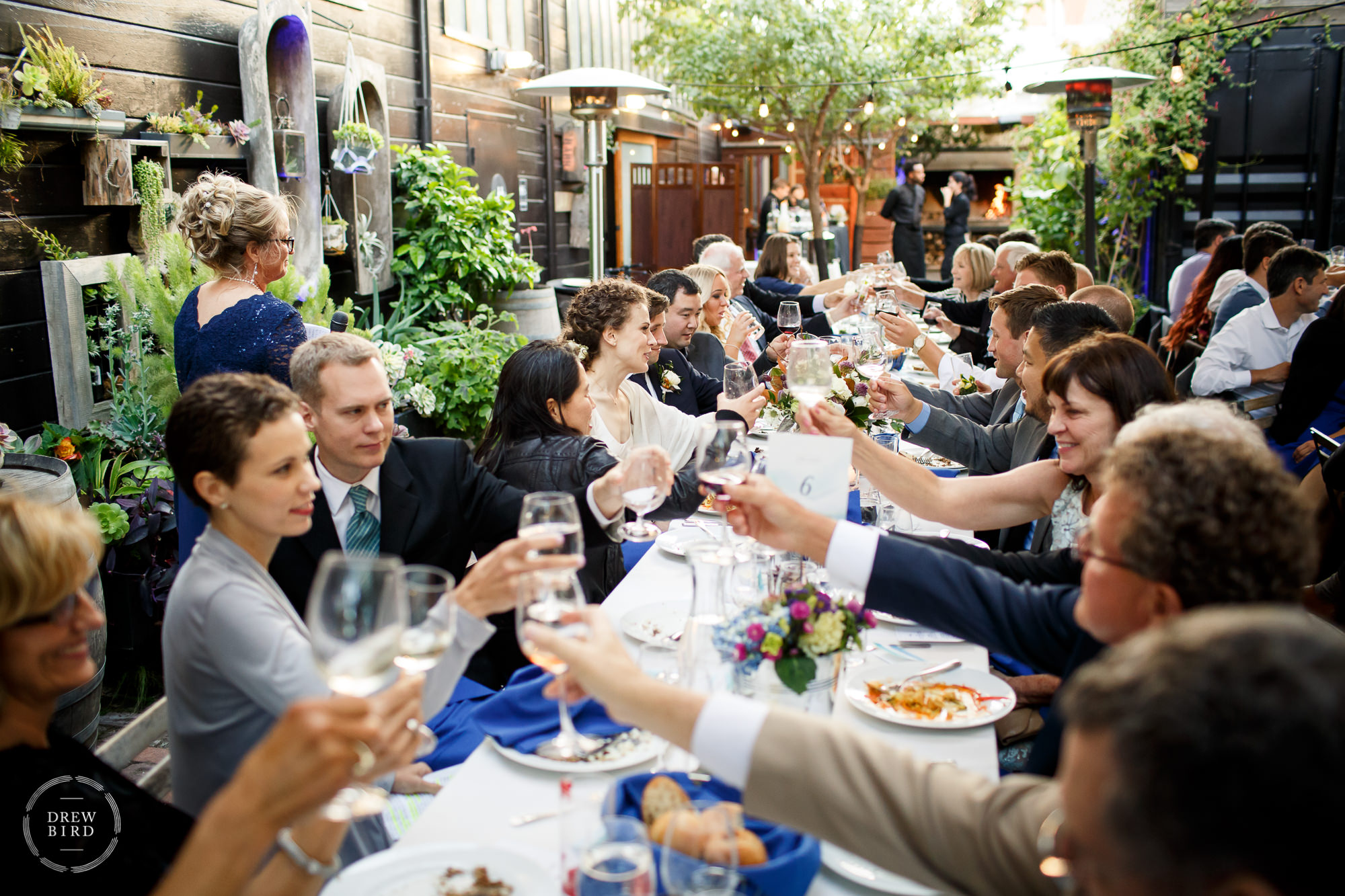 People raising glasses for cheers wiong table in an outdoor garden reception. Stable Cafe a San Francisco wedding venue.