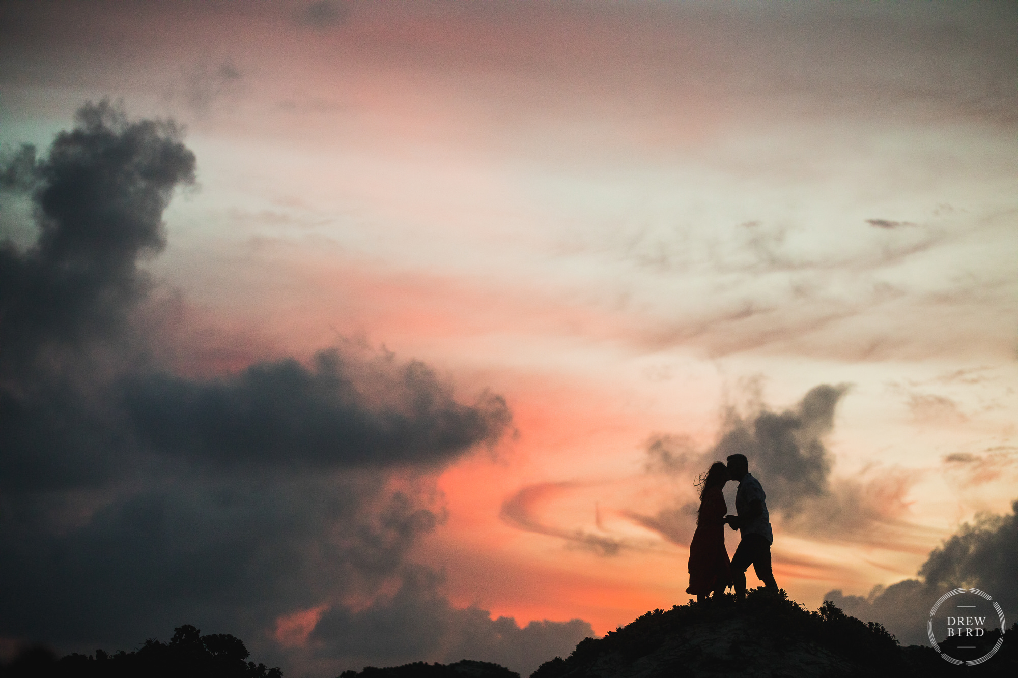 Silhouette of an Indian wedding bride and groom standing on sand dunes with sunset colors and a gorgeous sky. Destination wedding photography in Aruba by Drew Bird.