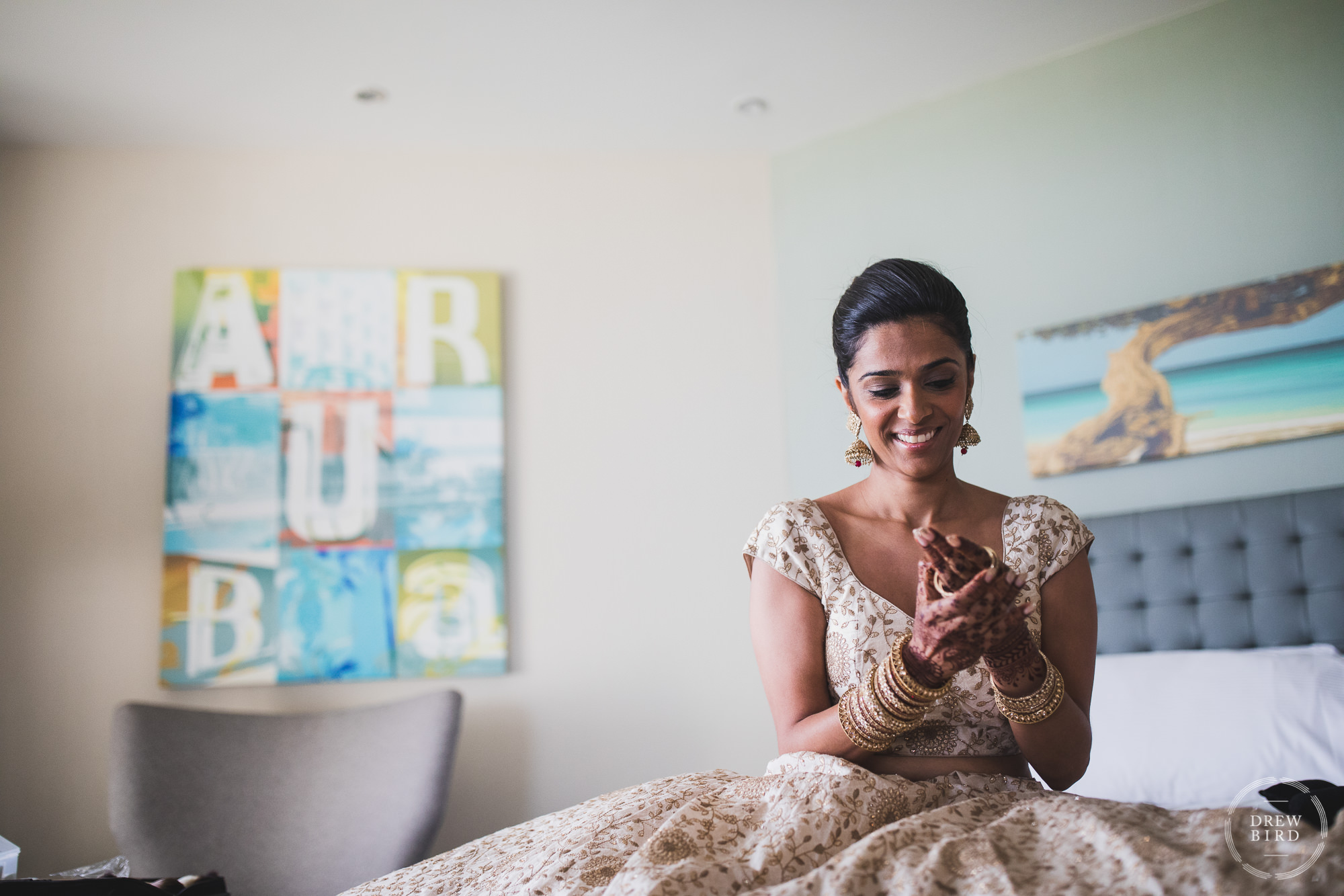 Indian wedding bride getting ready putting bracelets on her wrists. She is in her wedding dress and her hands are adorned with traditioanal henna painting. A professional wedding photography story by Drew Bird at the Hilton Aruba resort.