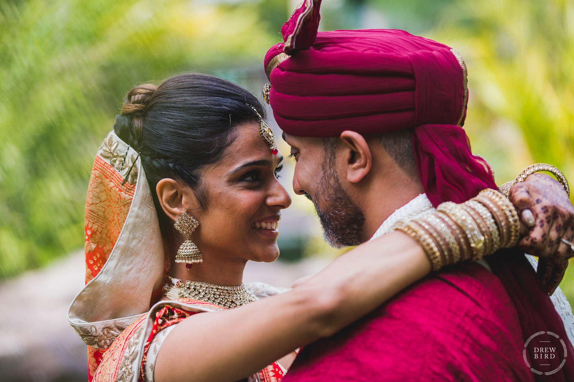 A close up photo of an Indian bride, in full traditional Hindu wedding attire and jewlery and henna painting, with her arms around the groom with their noses almost touching for an Indian wedding photography session on the beach in Aruba.