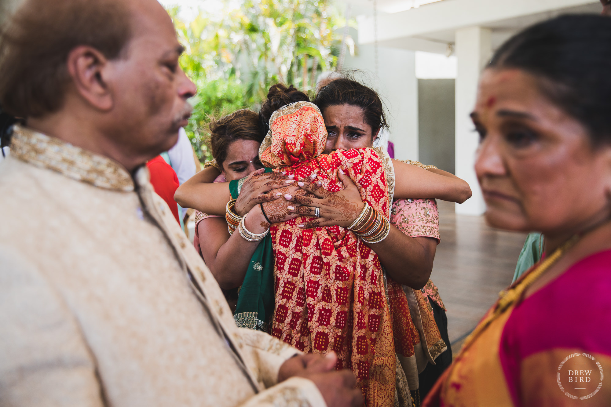 During the Vidiaa ceremony the bride embraces both of her sisters for a group hug. One of her sisters has tears in her eyes and the bride's parents are blurred out in the foreground during this Hindu wedding ceremony tradition. The moment is artistically and genuinely captured as a documentary style wedding photo by SF photographer Drew Bird who specializes in Indian and South Asian weddings. This is a destination Indian wedding in Aruba.