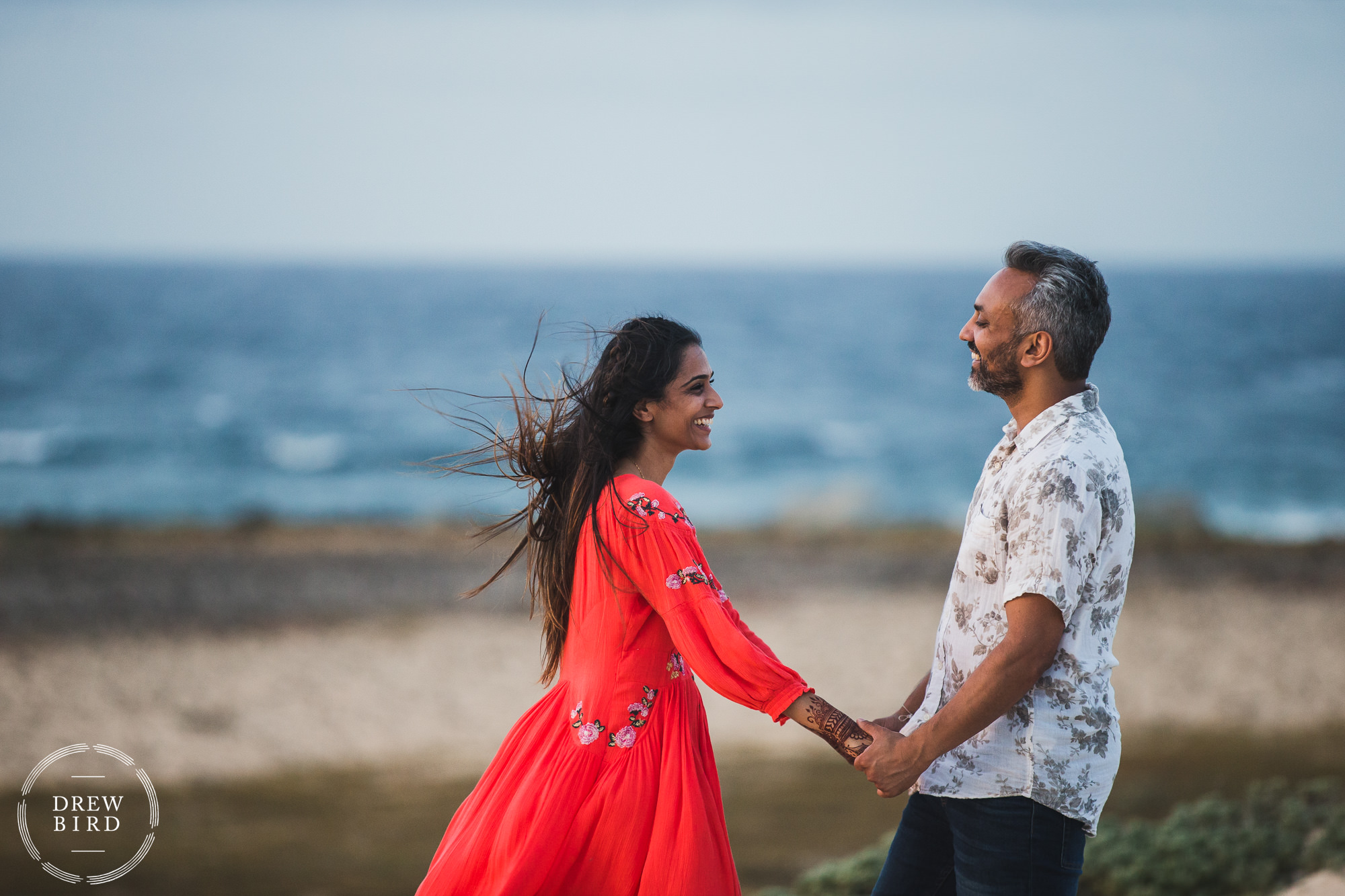 Indian wedding couple holding hands and laughing on a gorgeous empty beach for a destination wedding and adventure portrait session in Aruba by photographer Drew Bird.