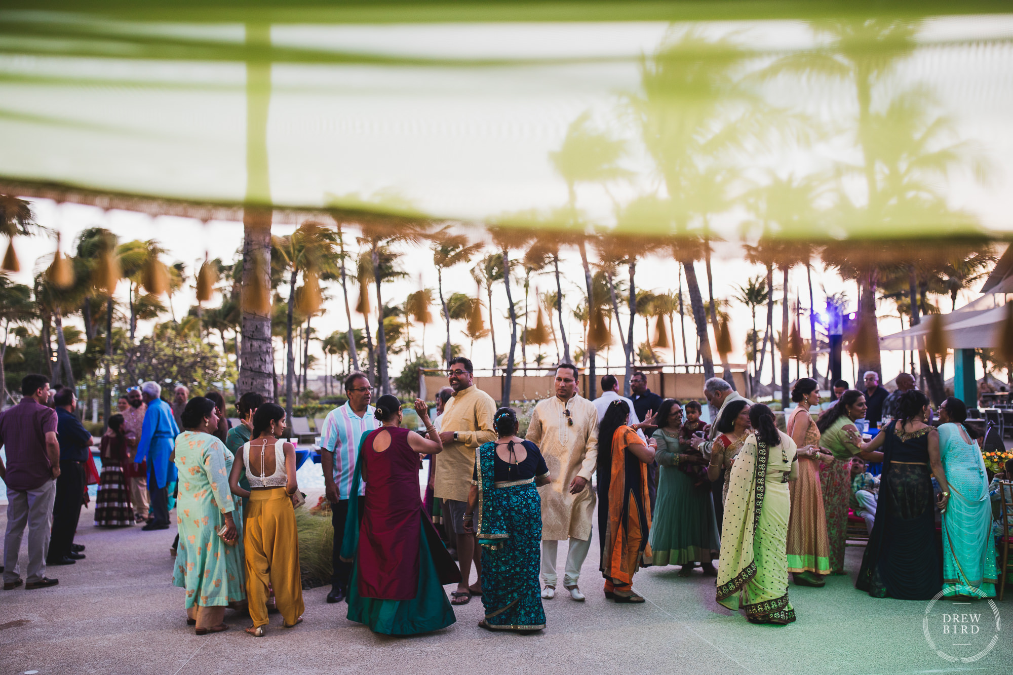 A large group of guests mingle next to the pool during happy hour at sunset for this destination Indian Hindu wedding welcome party at the Hilton Aruba Resort on the Caribbean island of Aruba.