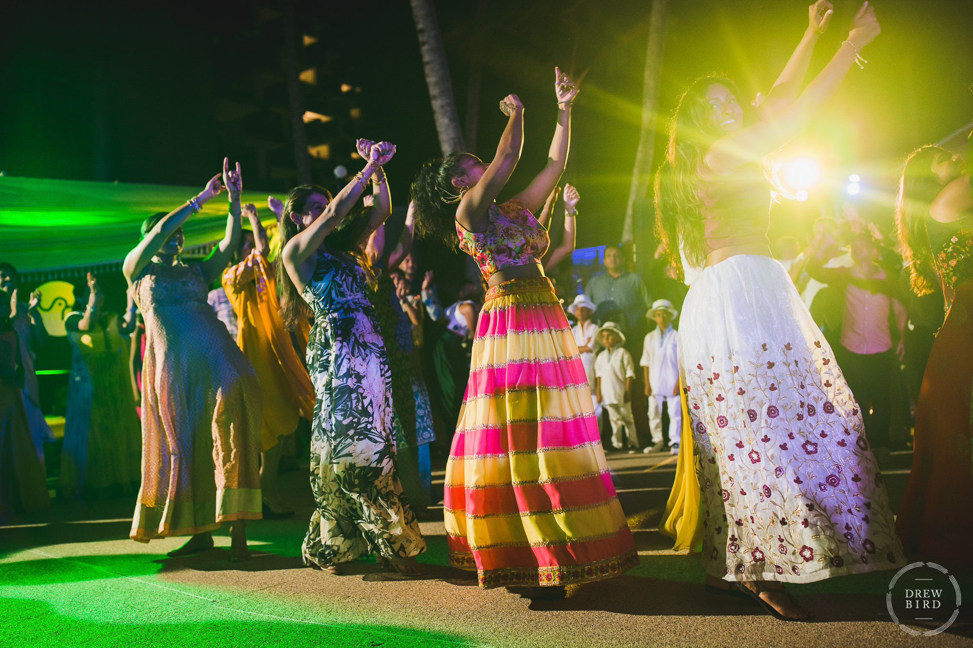 A group of family members perform a dance for the bride and groom and hundreds of guests with gorgeous colorful lighting at a fancy Indian and Hindu destination wedding at the Hilton Aruba Resort on the Caribbean island of Aruba. Images by San Francisco Indian Wedding Photographer Drew Bird.